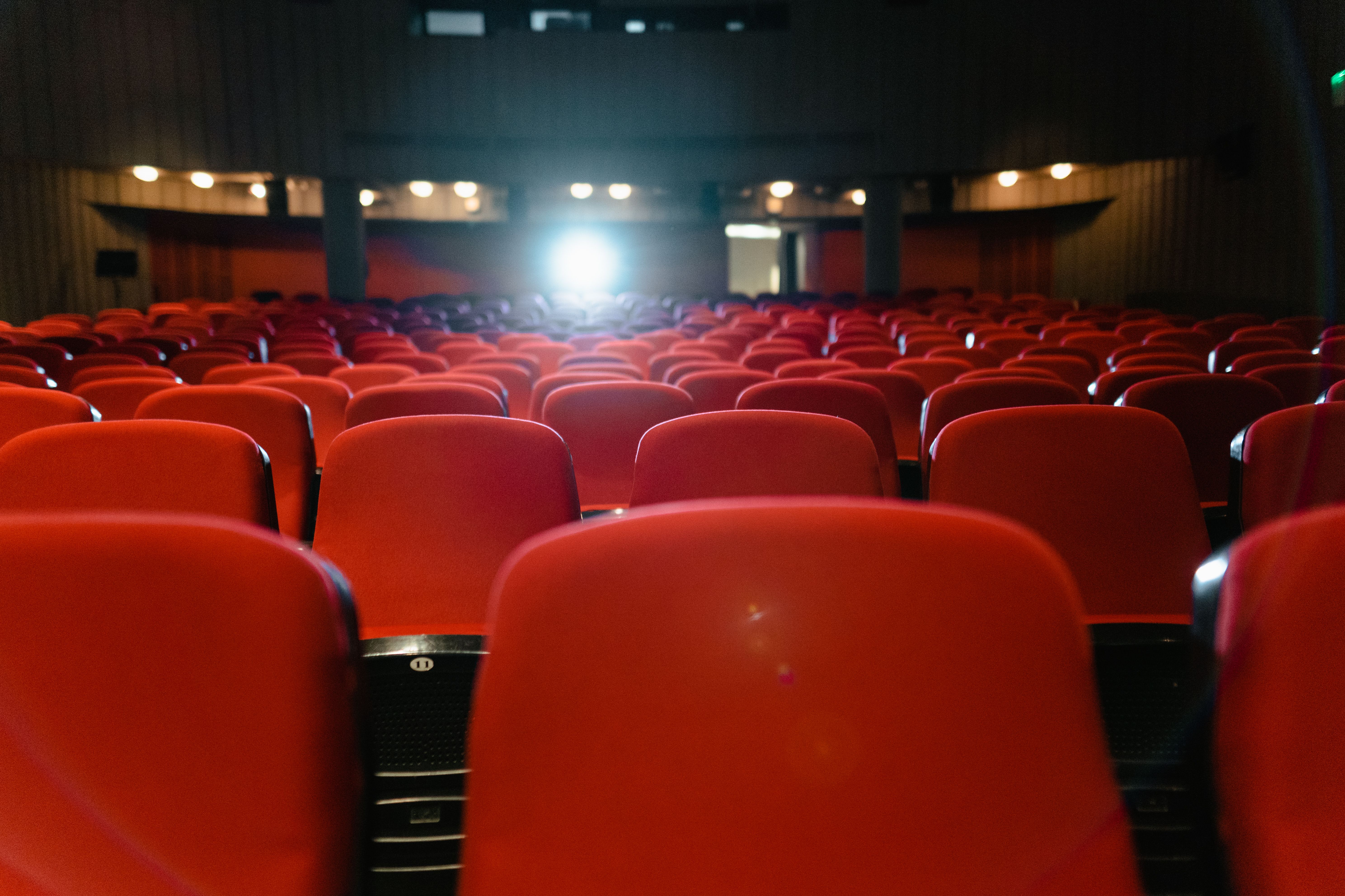A view of an empty cinema with rows of red seats facing the illuminated screen