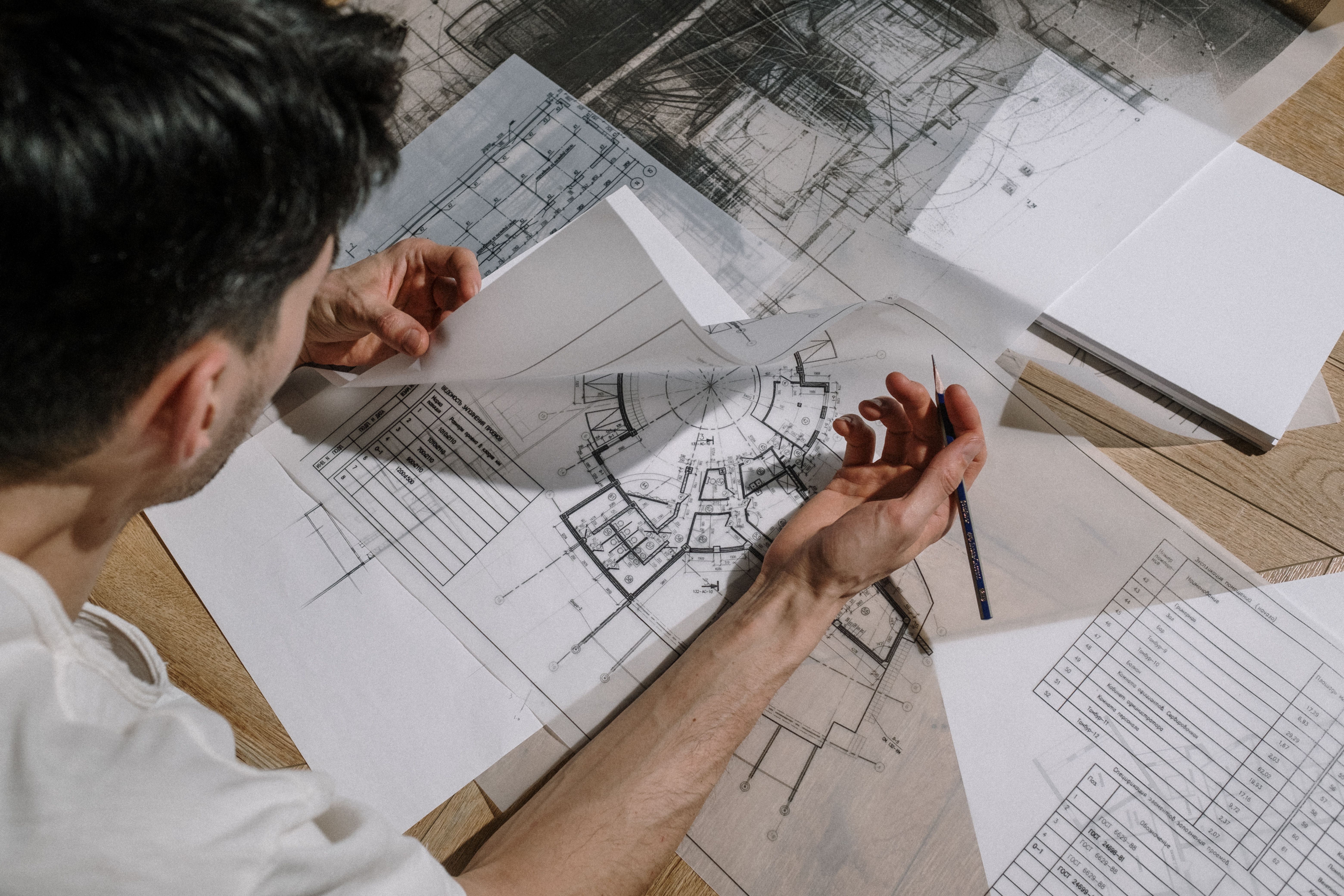 Architect studying and sketching over detailed blueprints indoors
