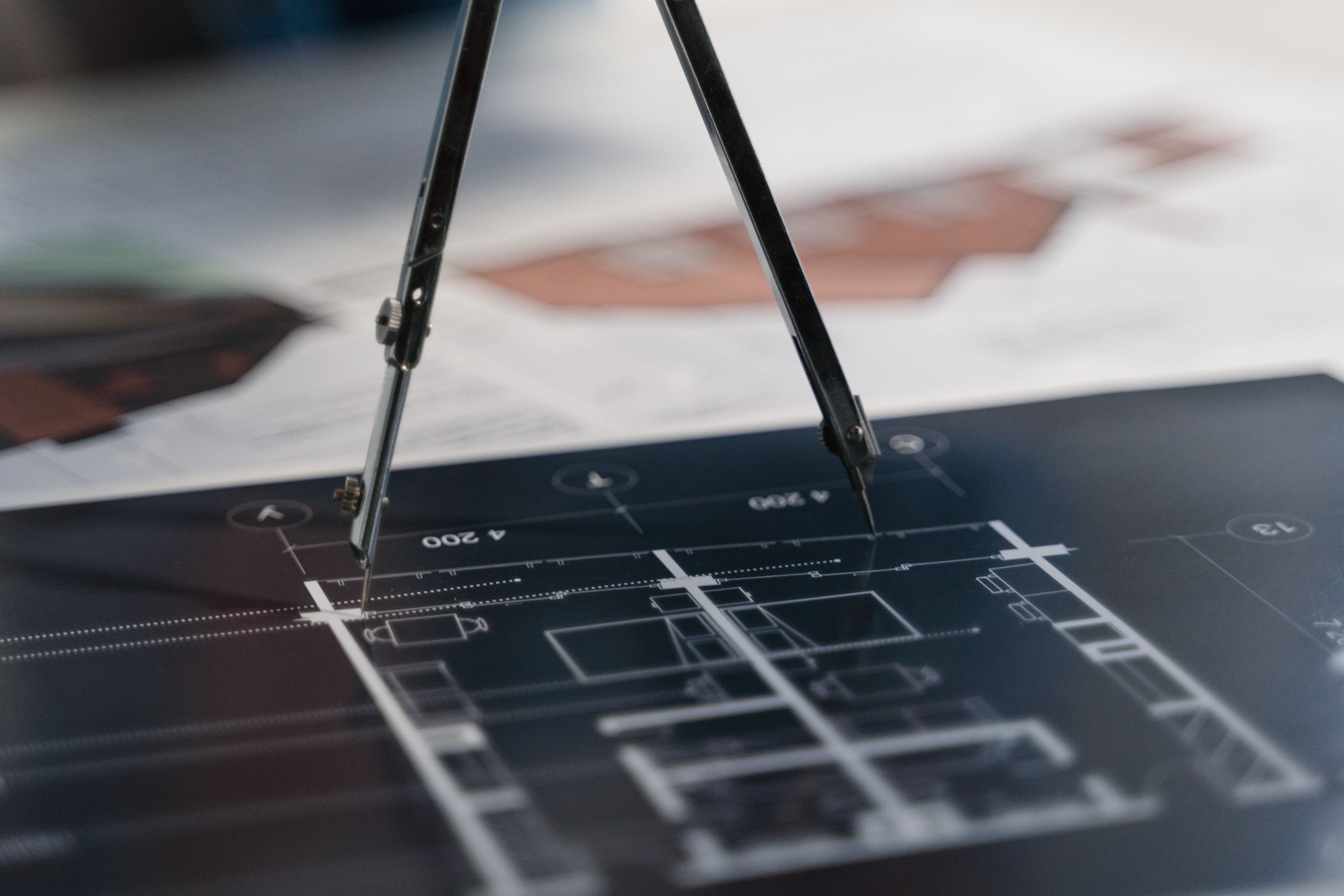 A compass resting on architectural blueprints showing planning and measurement details