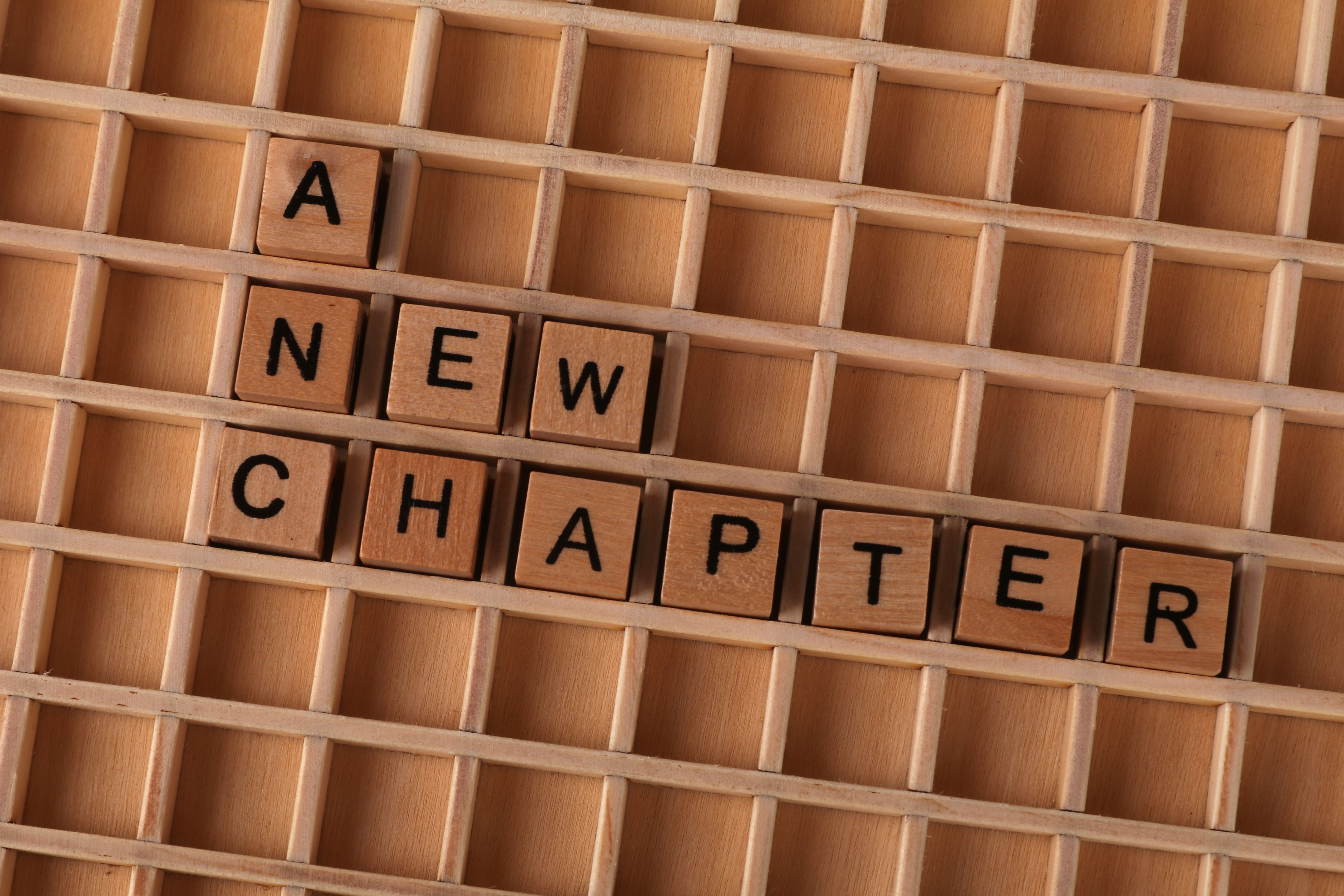Scrabble tiles spelling 'A New Chapter' on a wooden grid, symbolizing new beginnings