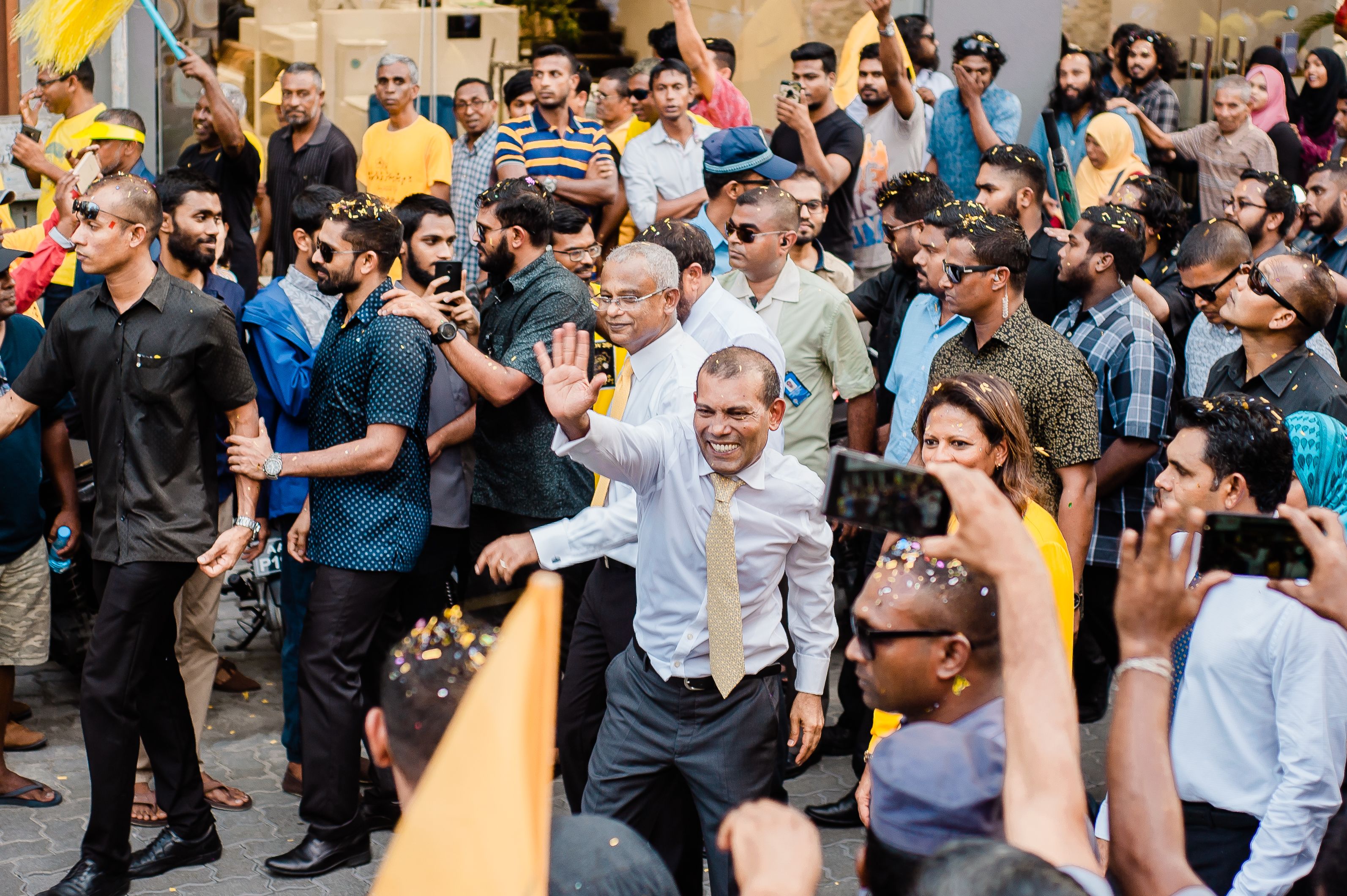 A politician waving to a crowd during a lively outdoor election campaign rally