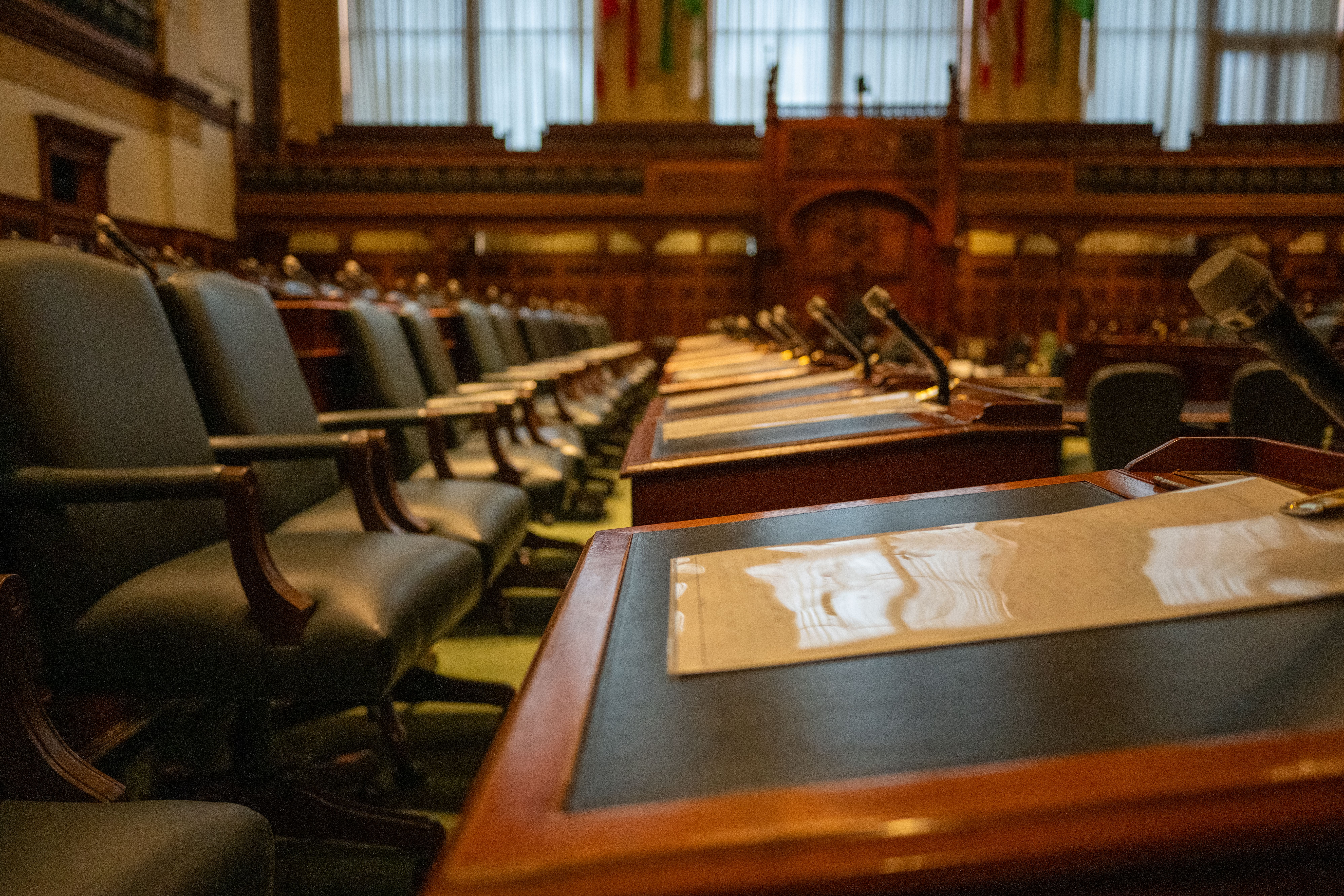 Empty legislative assembly chamber with rows of desks and microphones representing regional governance